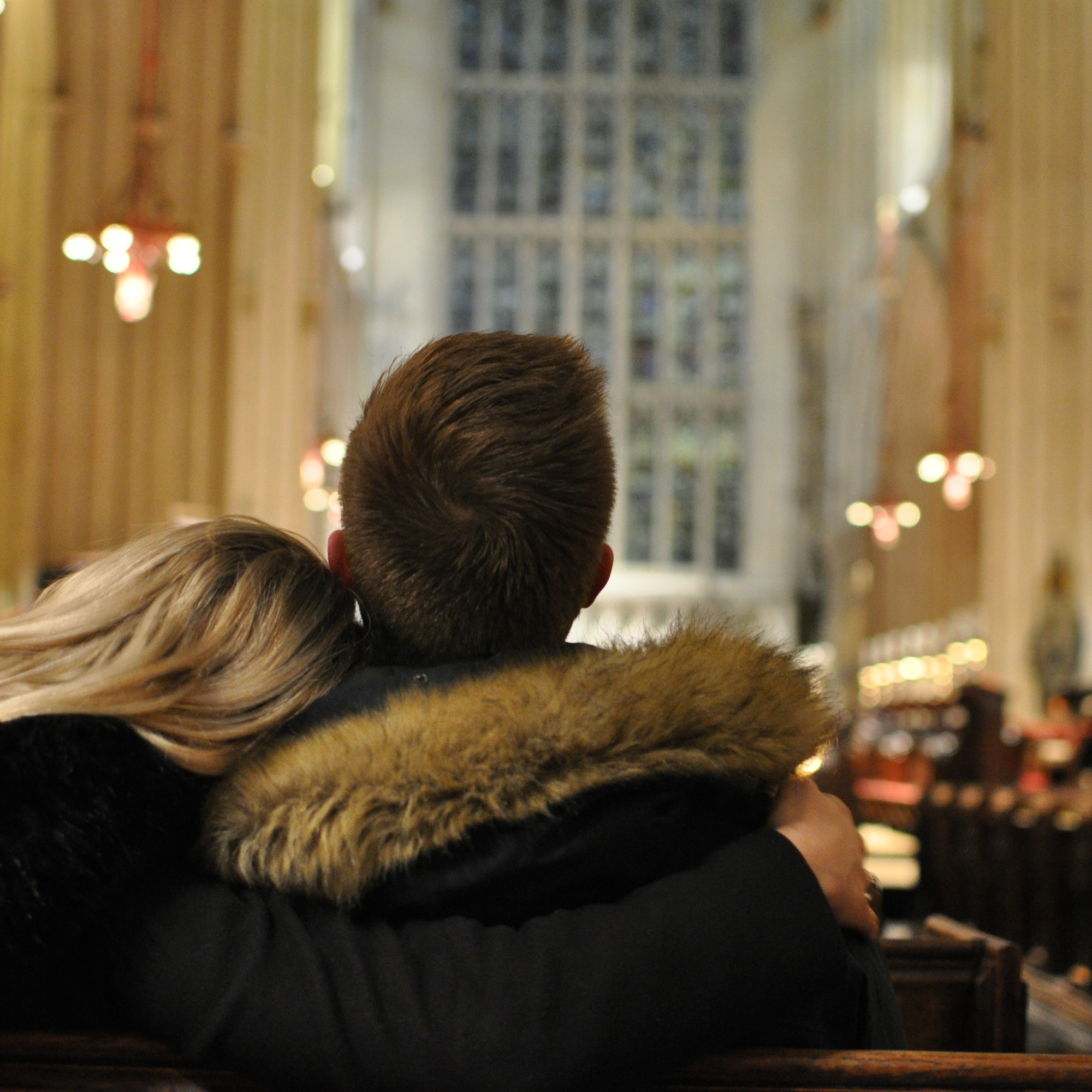 un couple de dos, elle la tête sur son épaule à lui, assis au fond d'une église toute illuminée